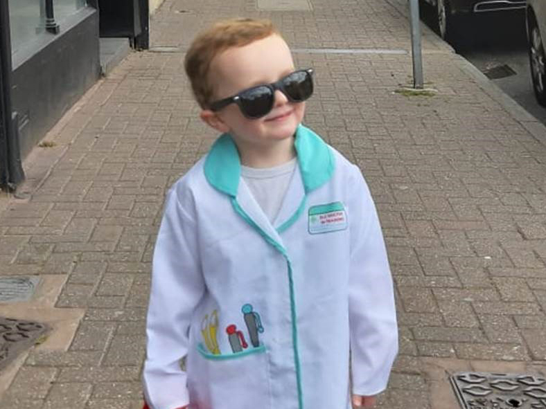 3-year-old fundraiser Hugo walks down the street dressed in a white doctor's coat.