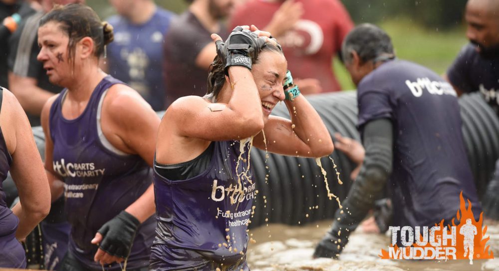 Woman covered in mud but grinning while taking on Tough Mudder