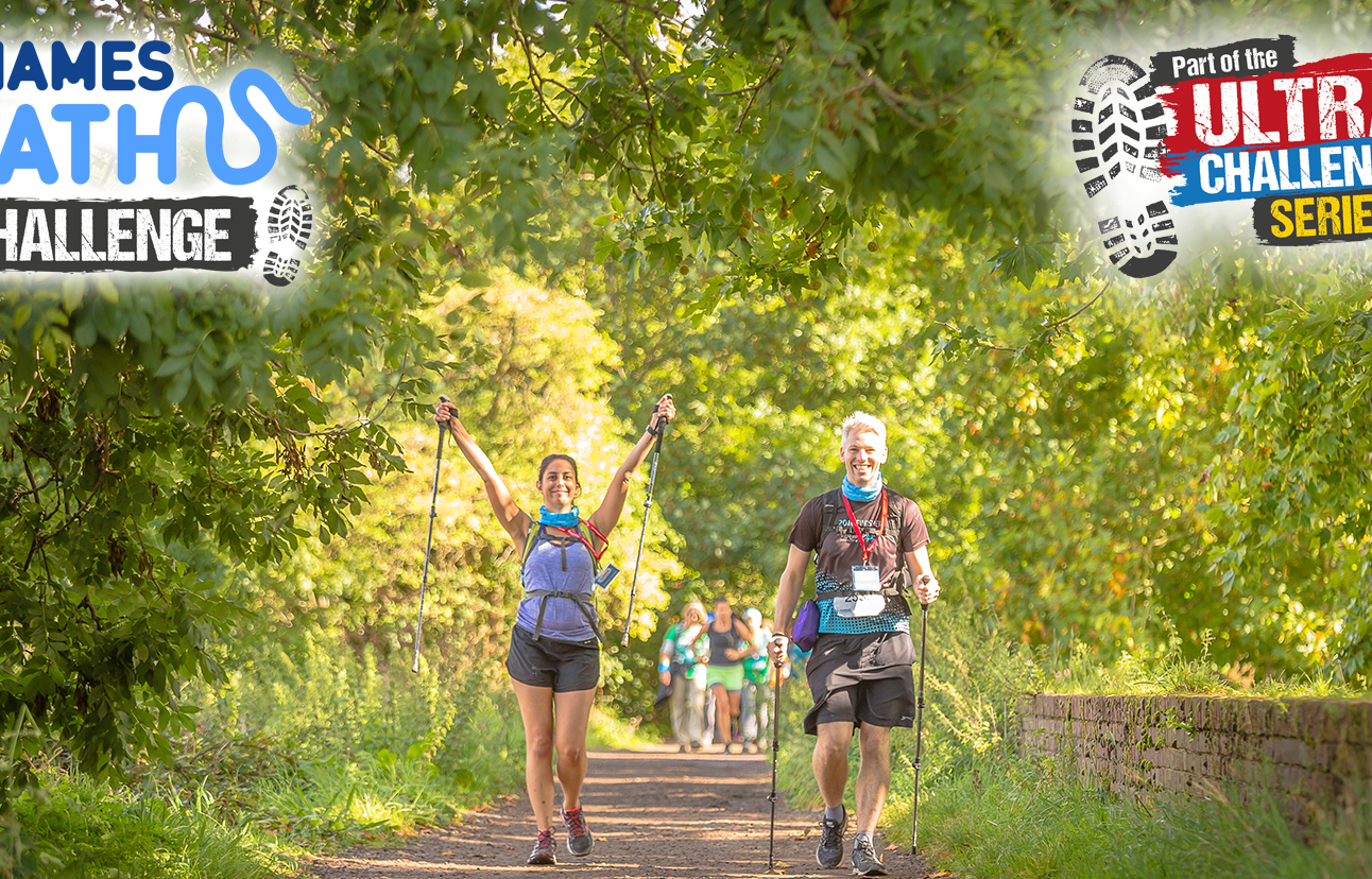 Two people in the middle of a green forest path in hiking gear with their arms raised