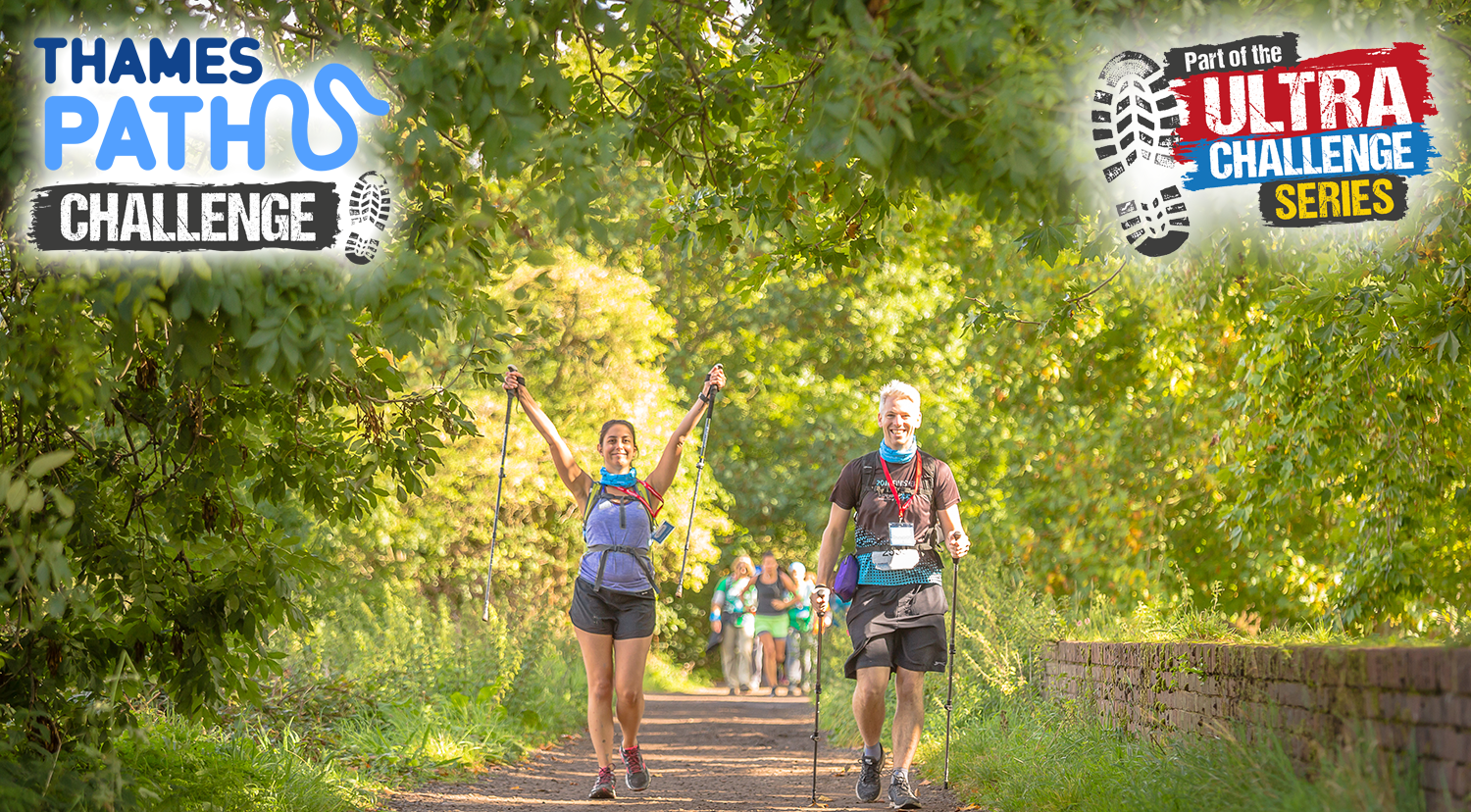 Two people in the middle of a green forest path in hiking gear with their arms raised