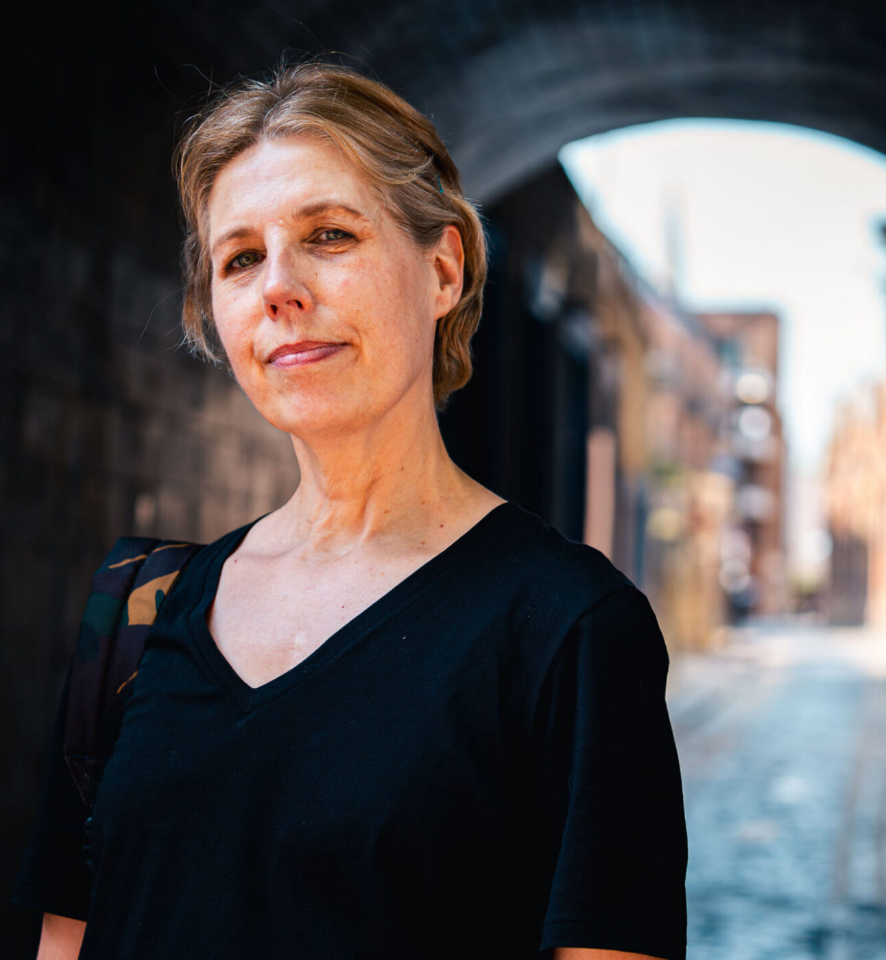 A woman standing in an alley, smiling to the camera wearing a black tshirt