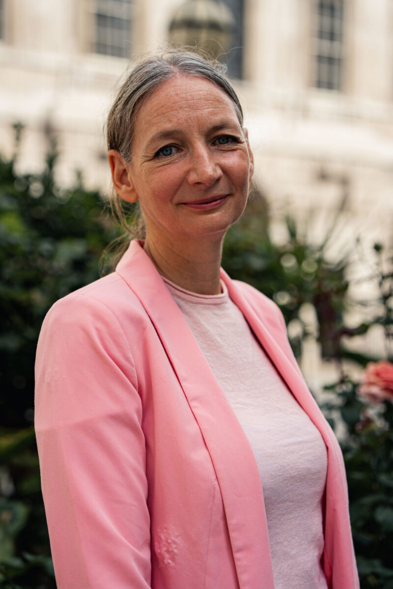 A woman wearing a pink blazer looking into the camera smiling.