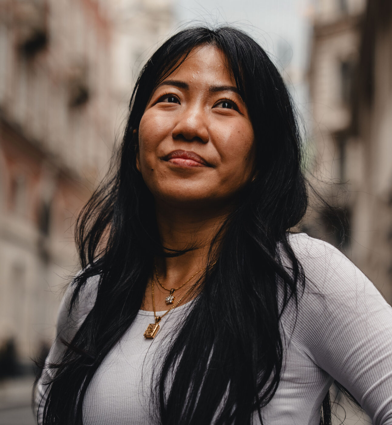 A close up of a woman in an urban setting, she's looking up from the camera slighly smiling.