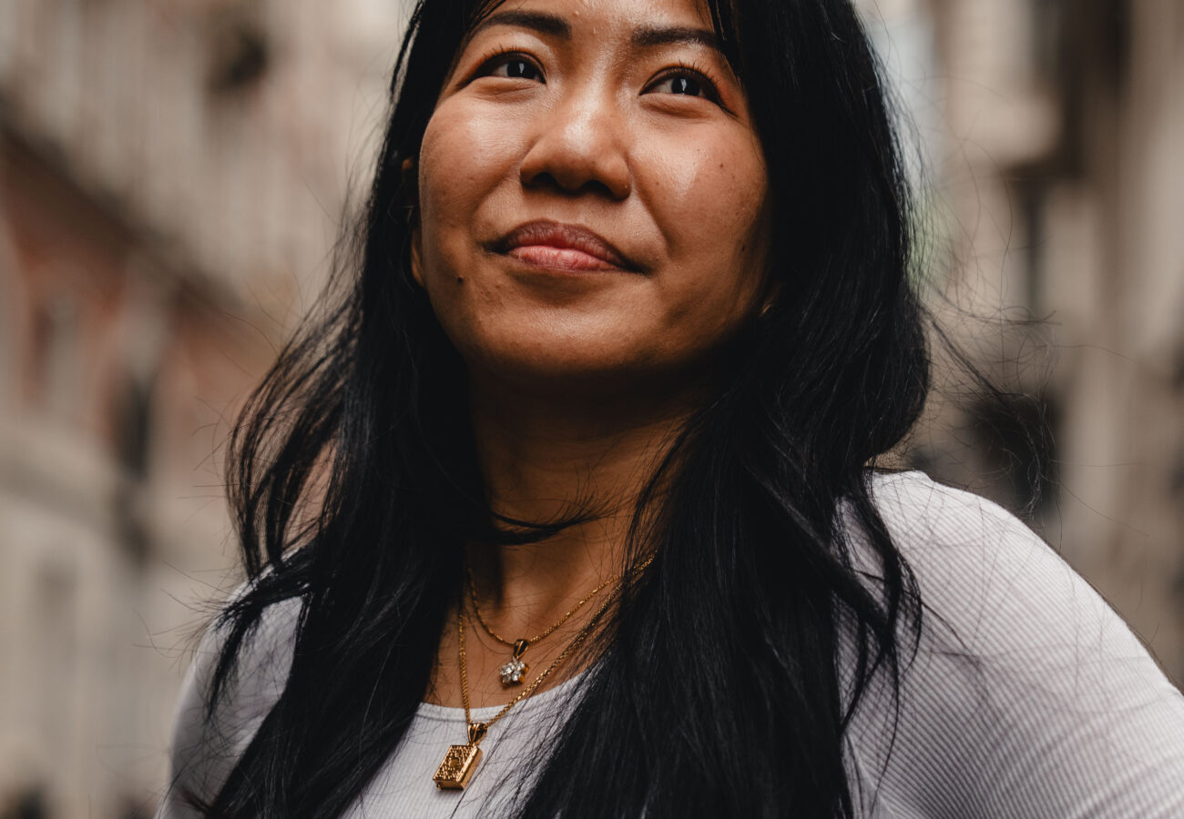 A close up of a woman in an urban setting, she's looking up from the camera slighly smiling.