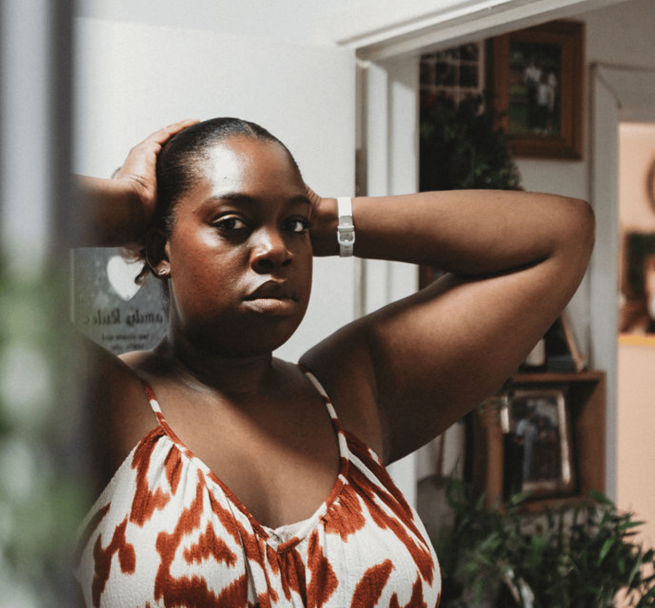 A woman in front of a mirror looking into the camera with her hands leaning on her head.