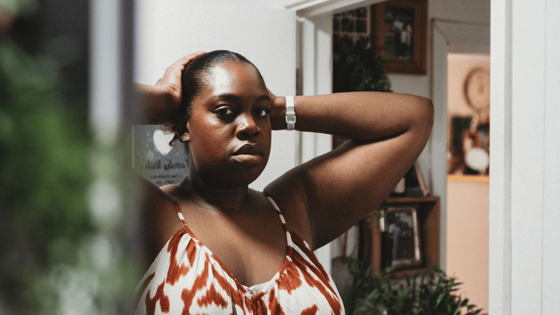A woman in front of a mirror looking into the camera with her hands leaning on her head.