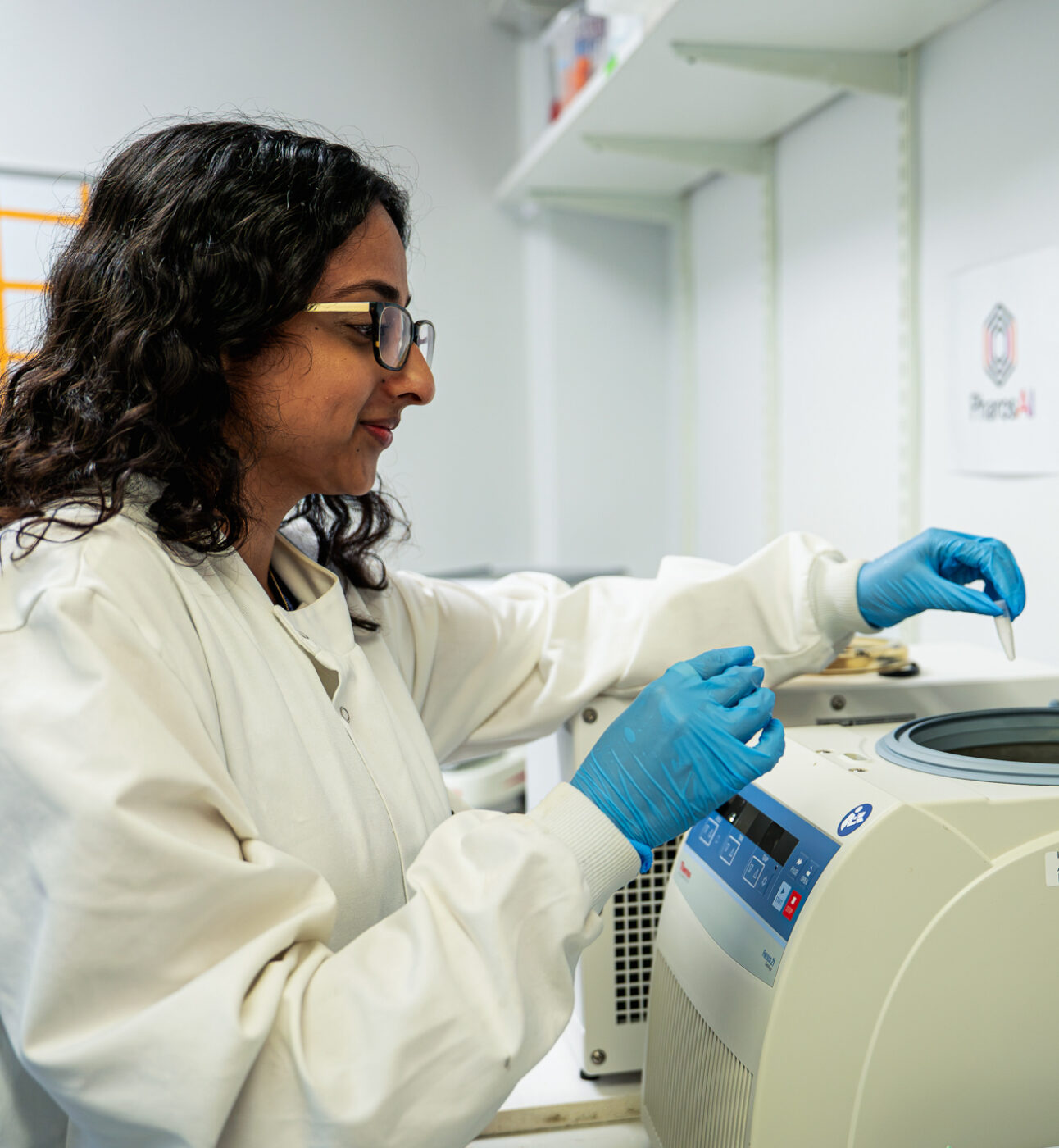 A female researcher in a lab, wearing a lab coat and lab gloves, holding a pipette. Research lab in the background.