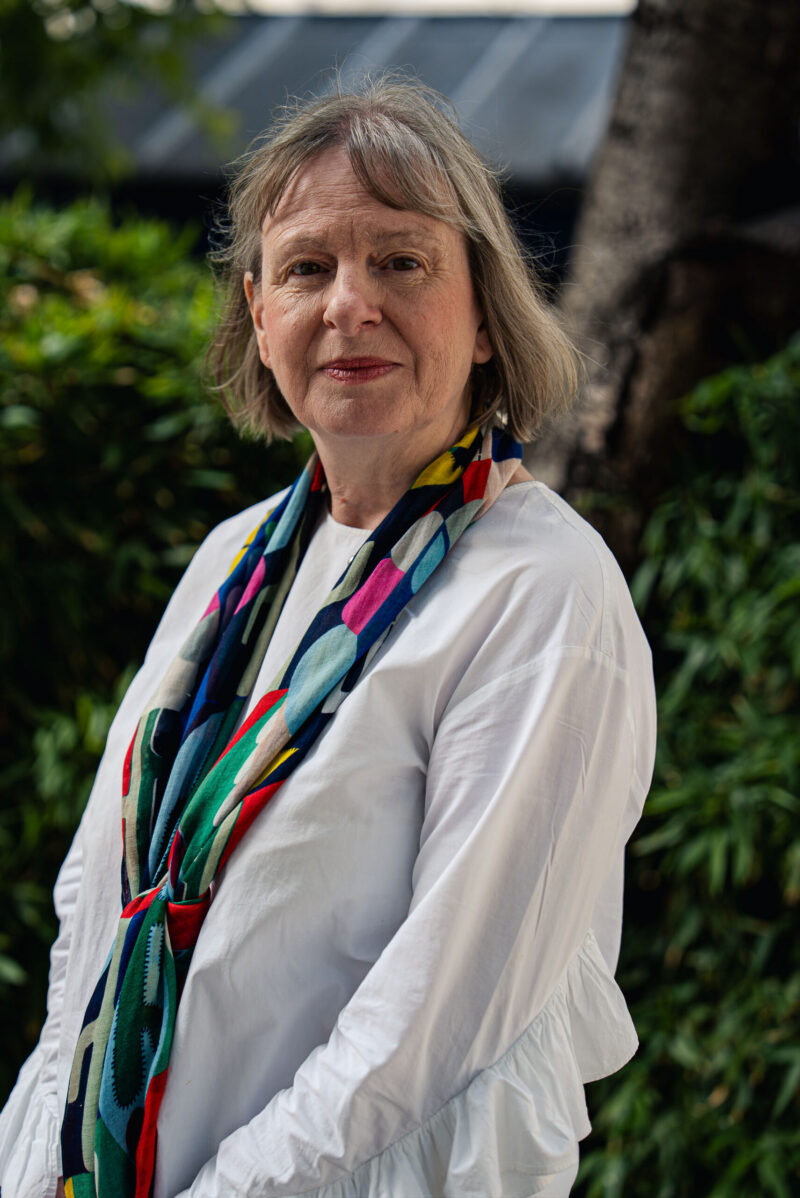 A woman looking into the camera wearing a white top and a colorful scarf around her neck
